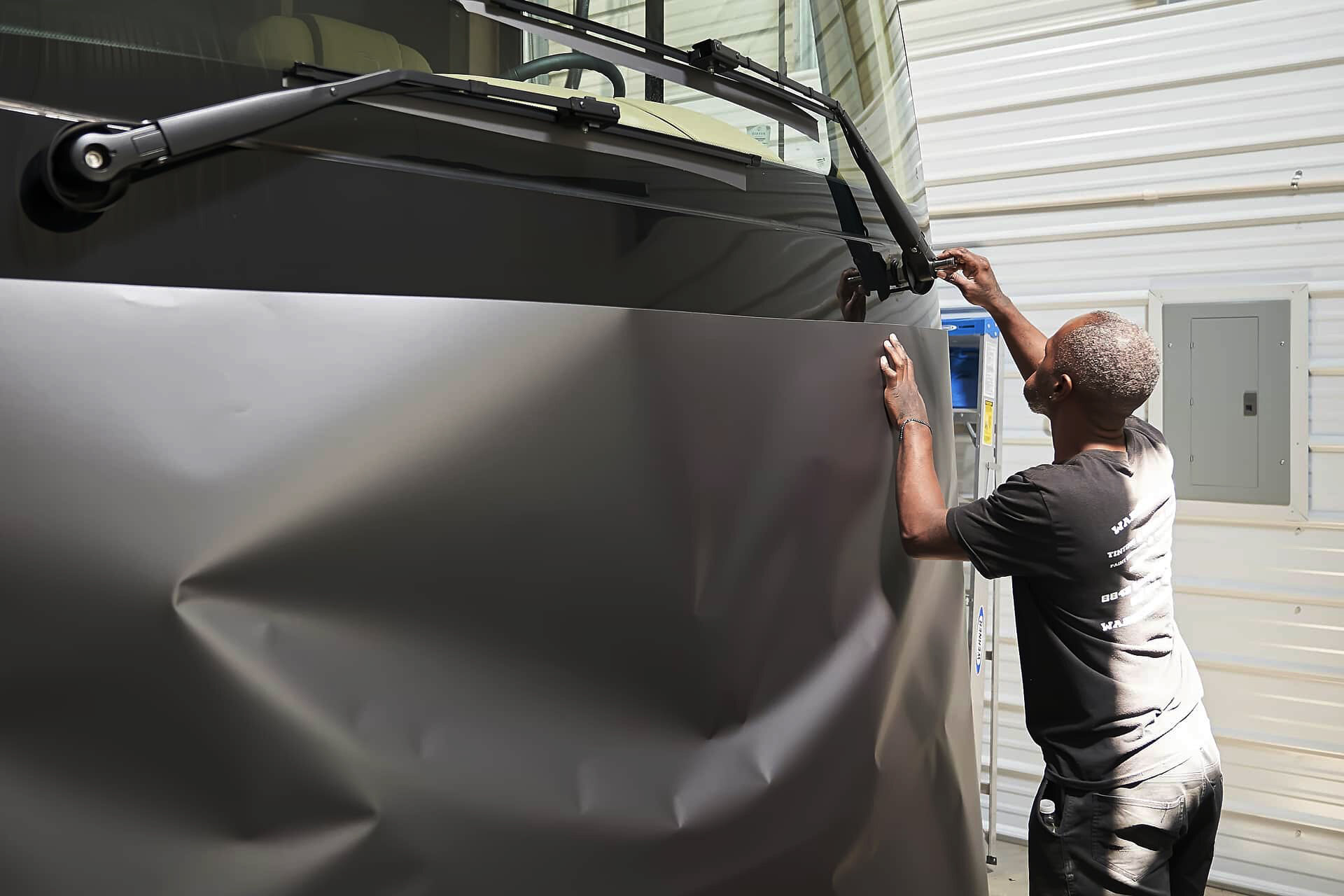 Installer positioning a large vinyl panel on the front of a Tiffin motorcoach (project photo 120)