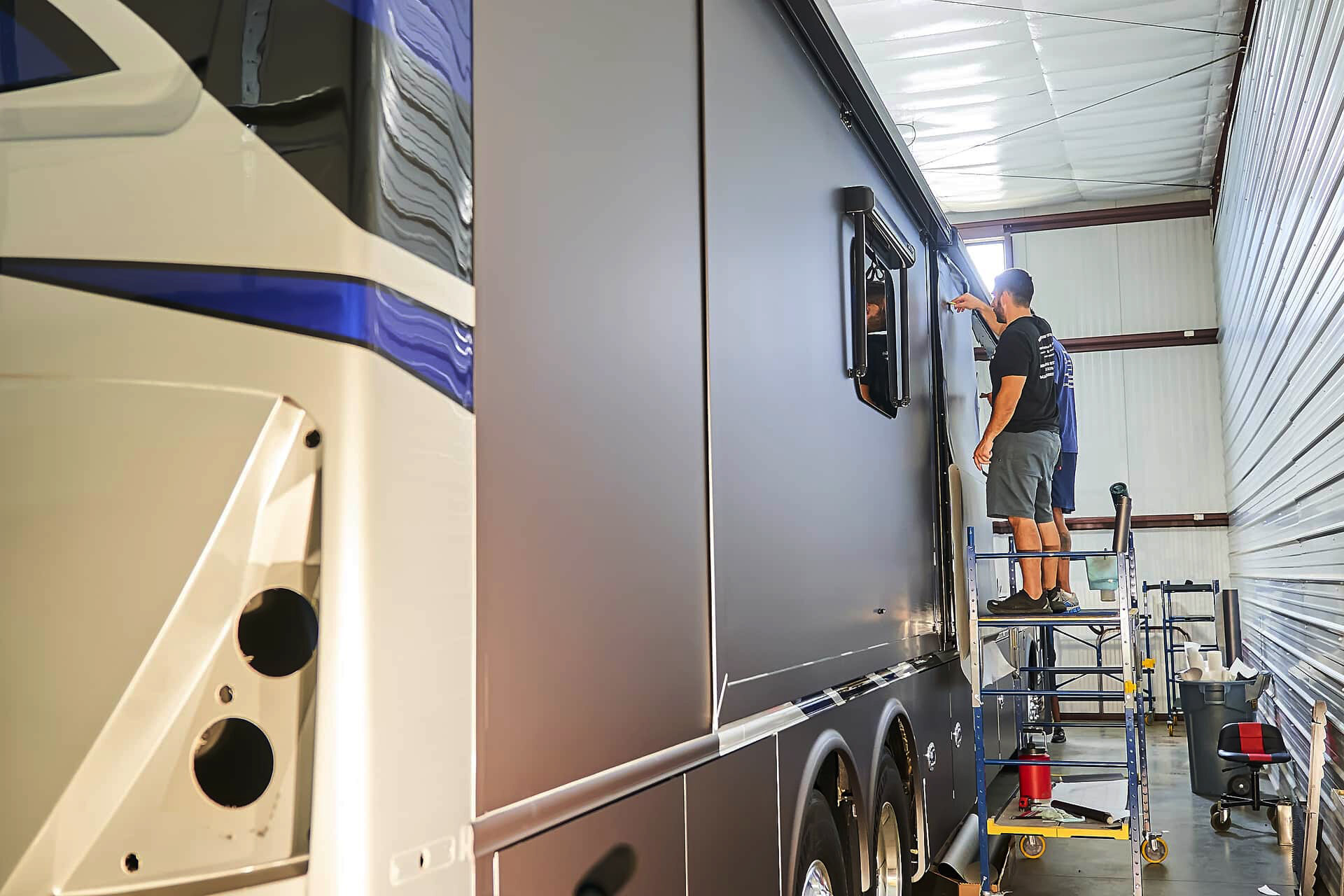 Wide view of vinyl wrap installation progressing along the motorcoach side (project photo 129)
