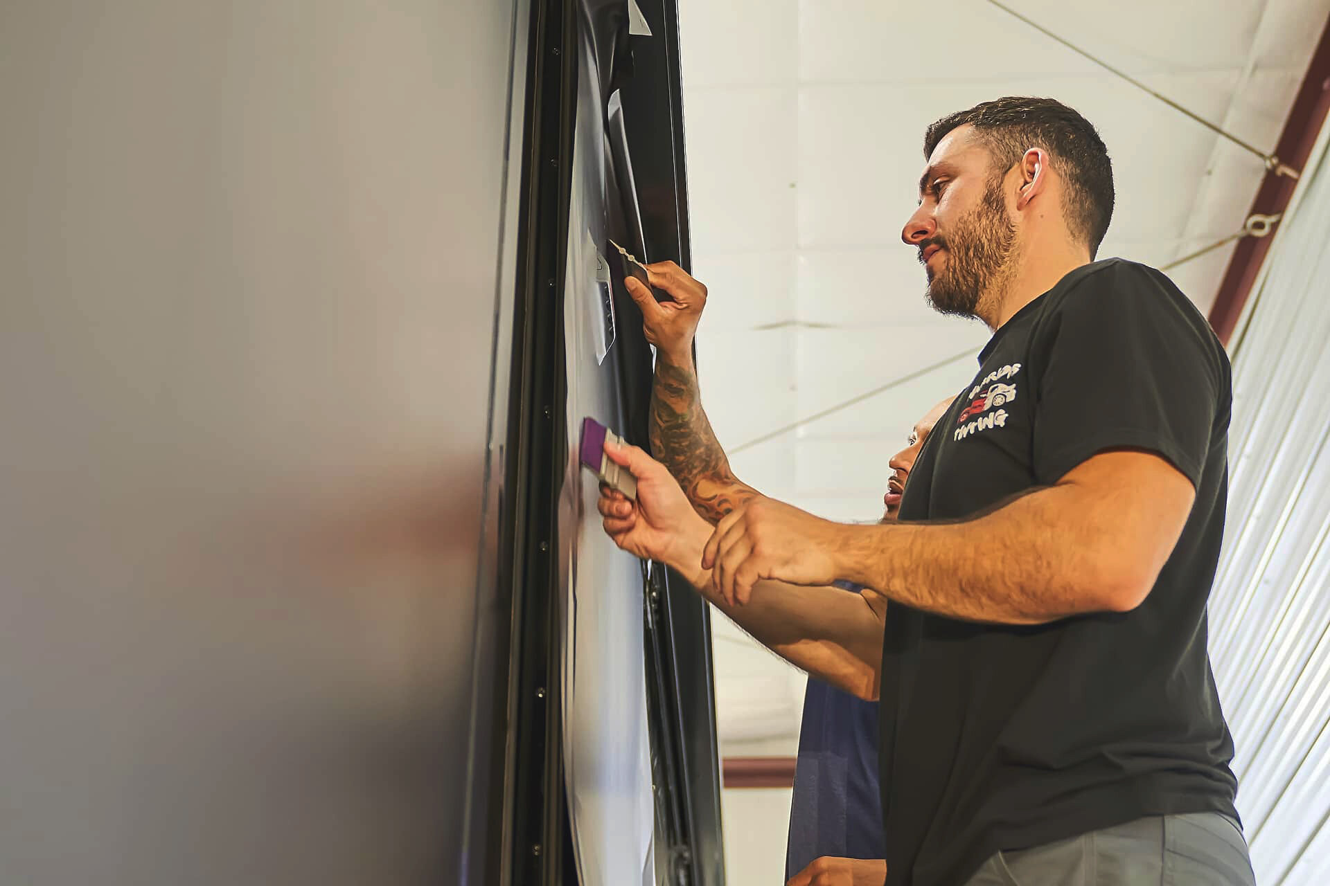 Technician precision-trimming vinyl along a motorcoach panel edge (project photo 134)