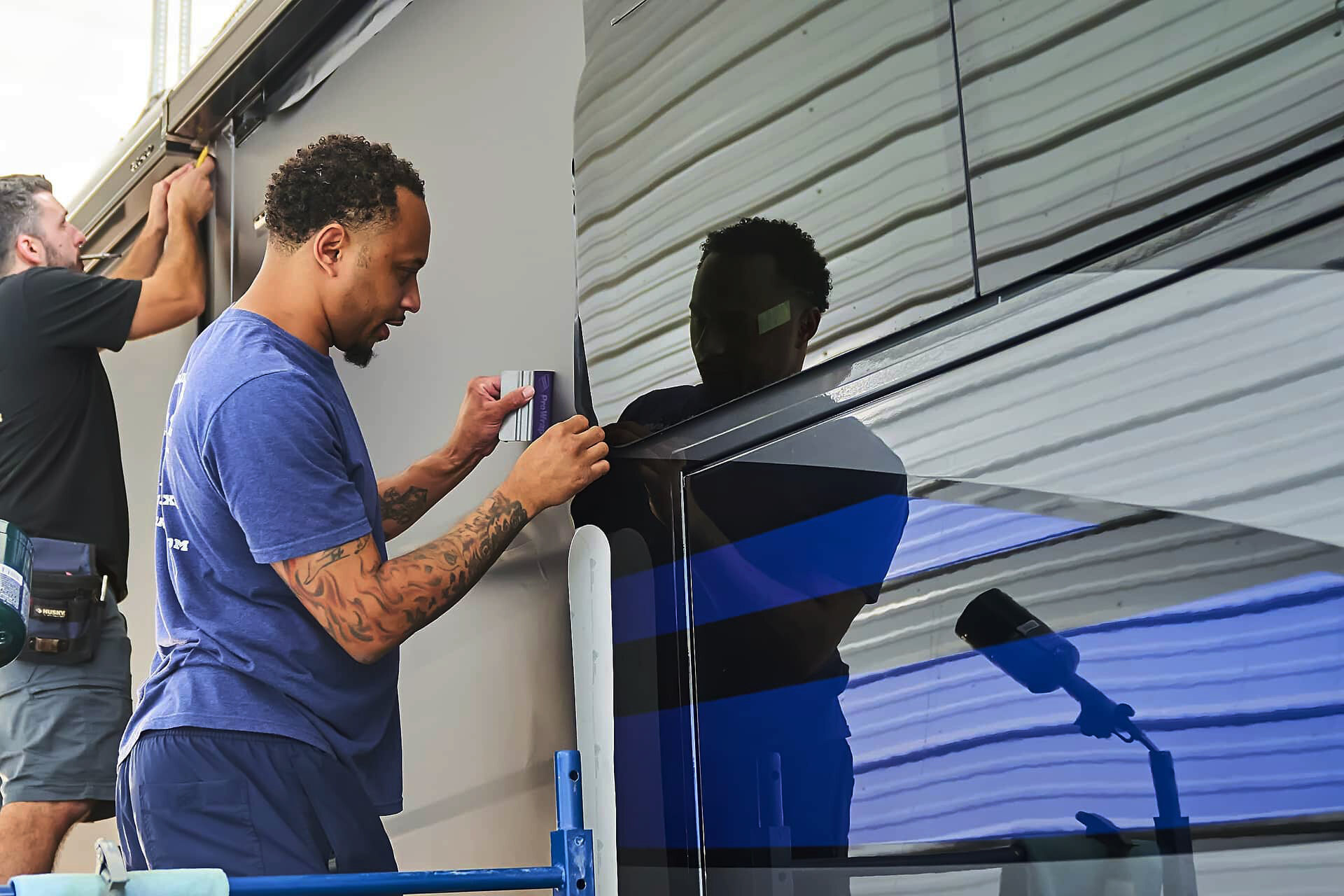 Technicians finishing vinyl edges around a motorcoach window and body panel (project photo 151)