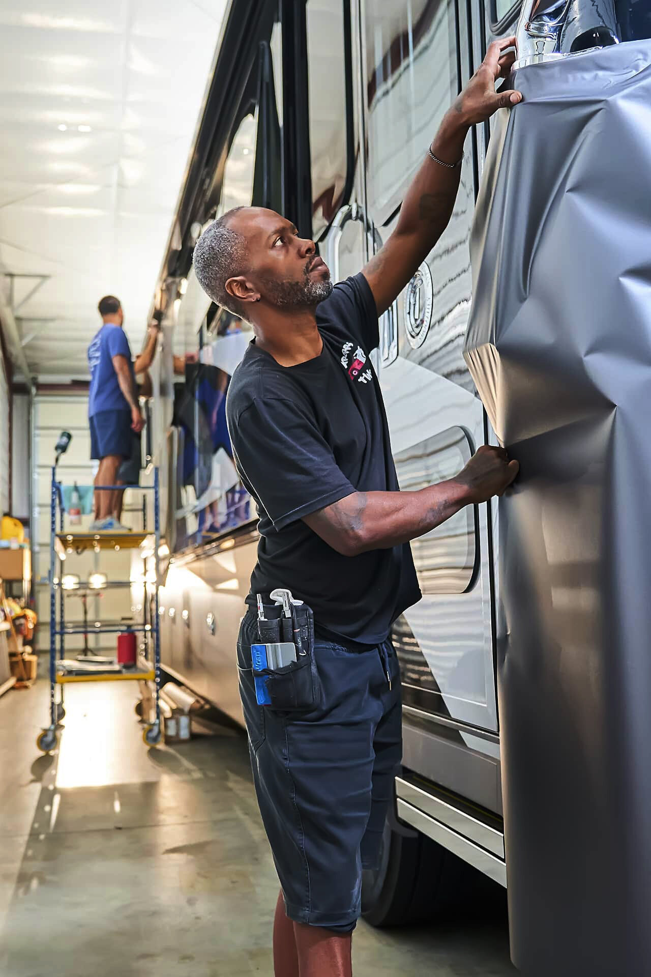 Technician fitting vinyl around the front corner of a Tiffin motorcoach (project photo 165)