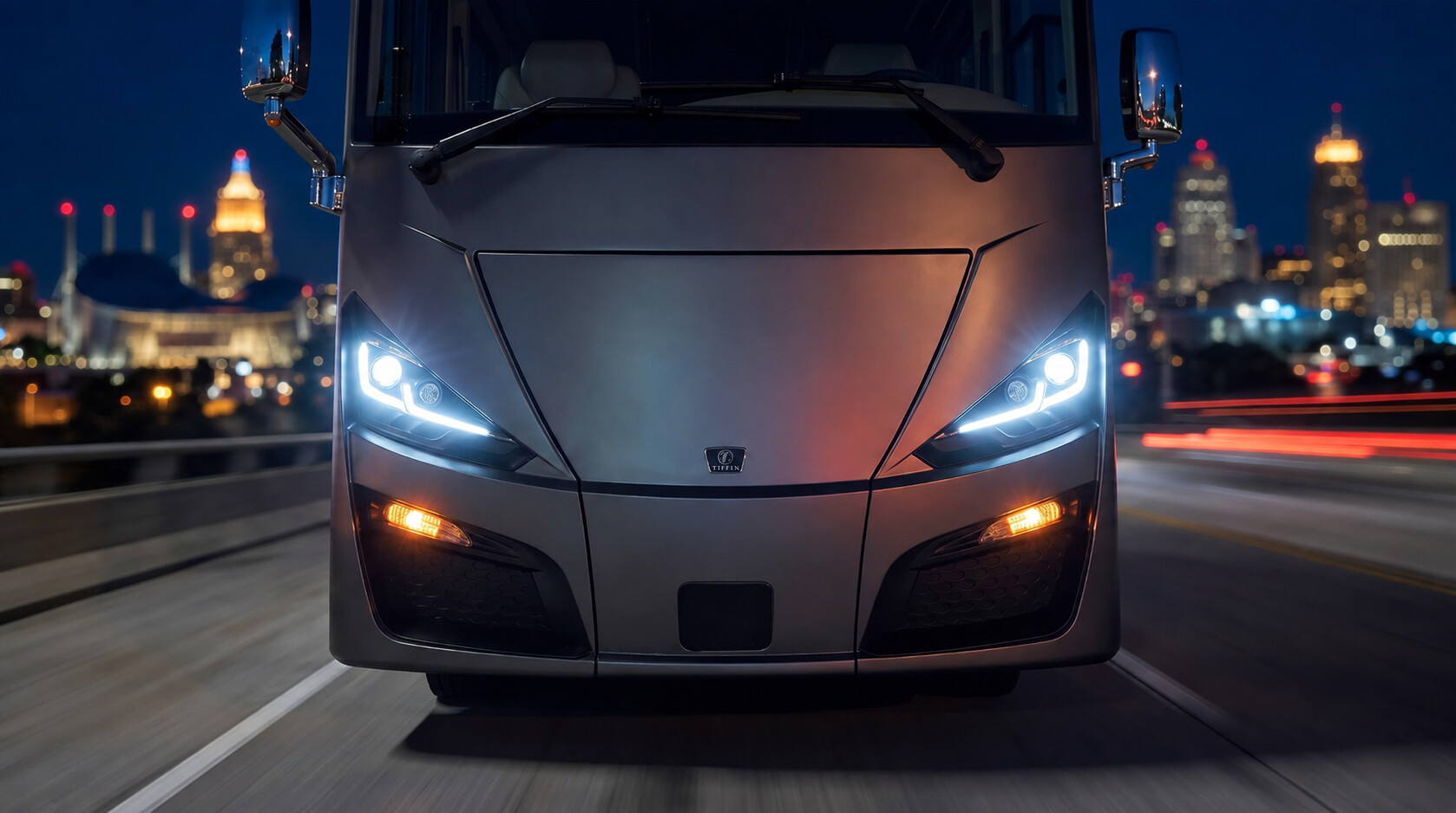 Front view of a Tiffin motorcoach against the Kansas City skyline at night